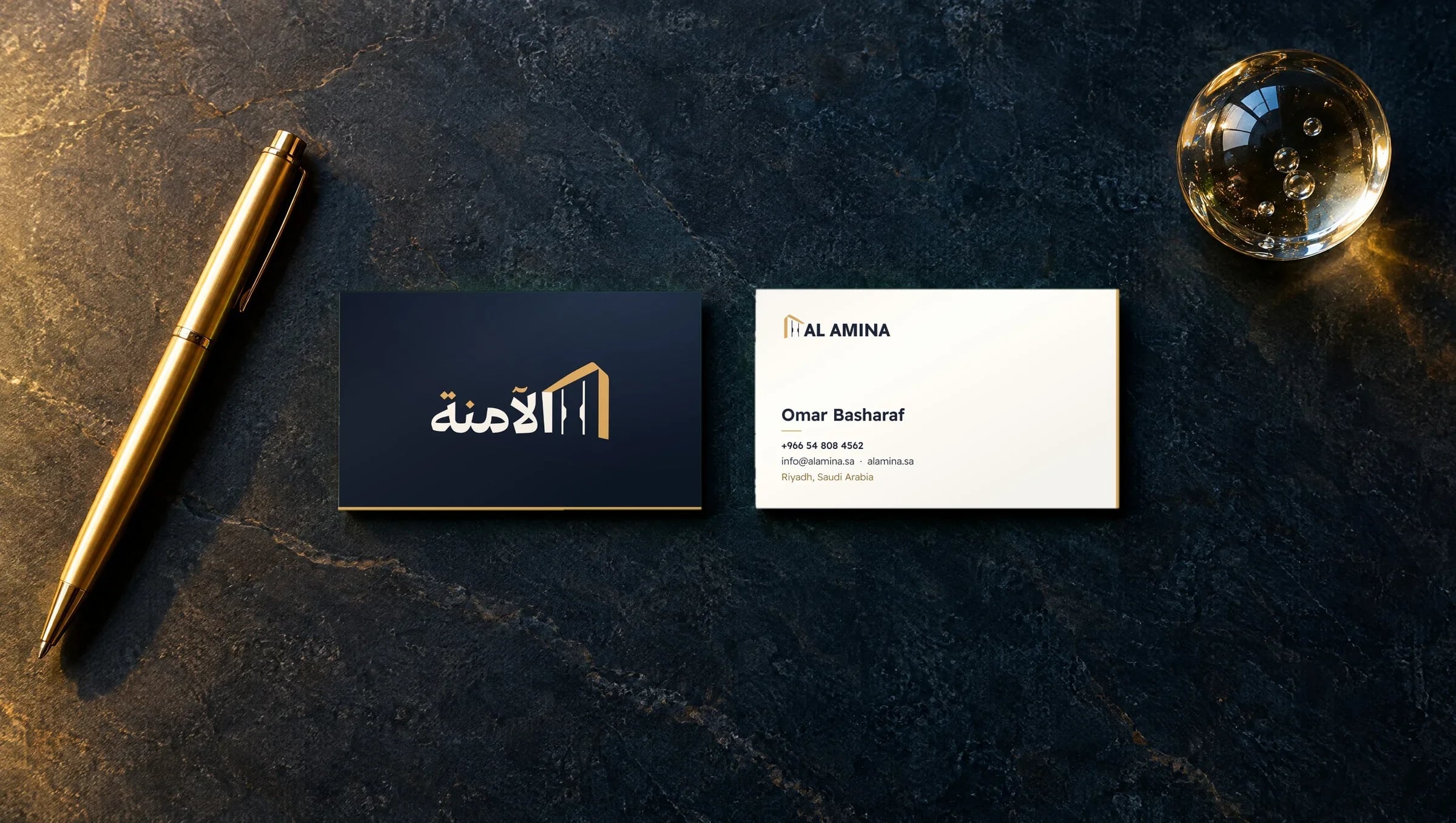 Alamina business cards on dark stone: the Arabic logo on navy, the English lockup on ivory
