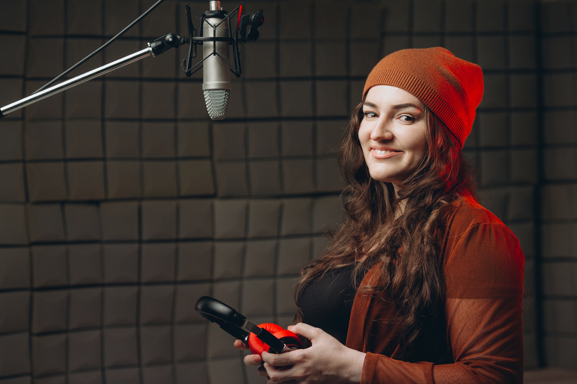 Young woman in headphones emotionally singing in microphone in the sound recording studio.